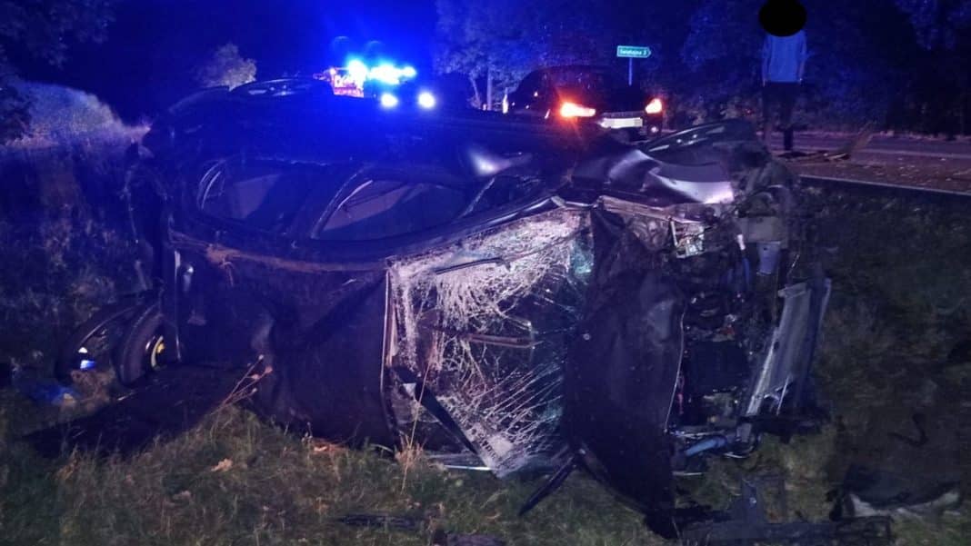Rozbity samochód w rowie na drodze krajowej, uszkodzenia karoserii i rozbite szyby, nocą.