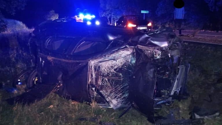 Rozbity samochód w rowie na drodze krajowej, uszkodzenia karoserii i rozbite szyby, nocą.