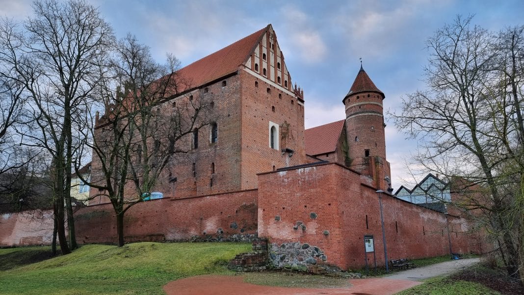 Widok na zamek kapituły w Olsztynie z ceglaną architekturą i otaczającym parkiem.