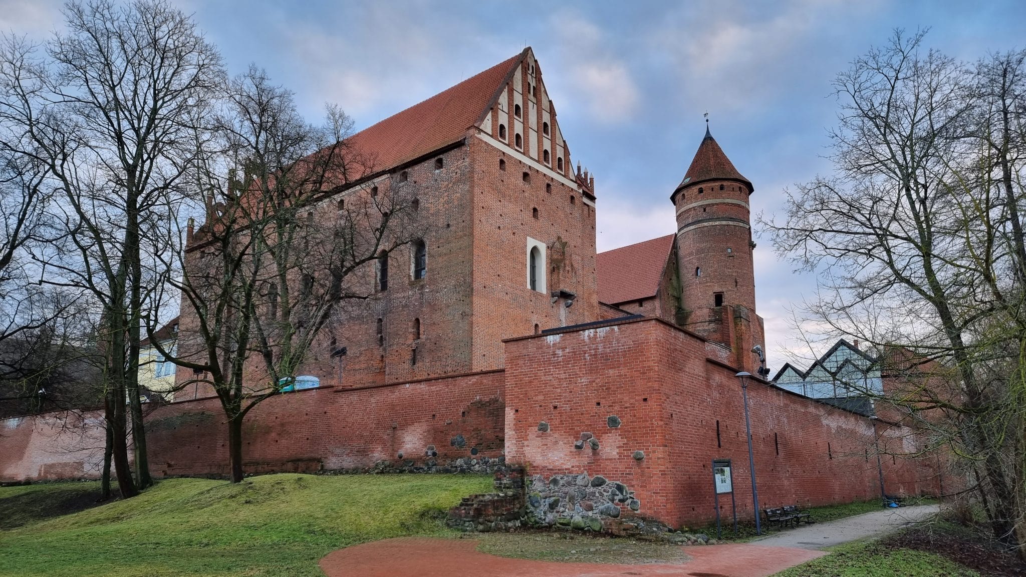 Widok na zamek kapituły w Olsztynie z ceglaną architekturą i otaczającym parkiem.
