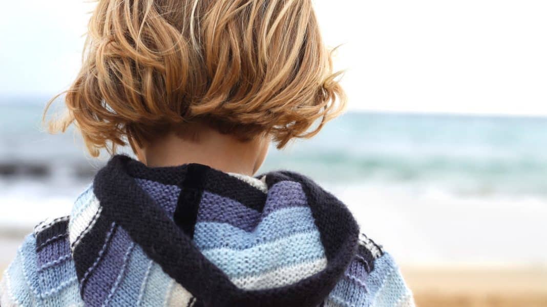 Kobieta z krótkimi, blond włosami patrzy w dal na plaży, widok od tyłu.