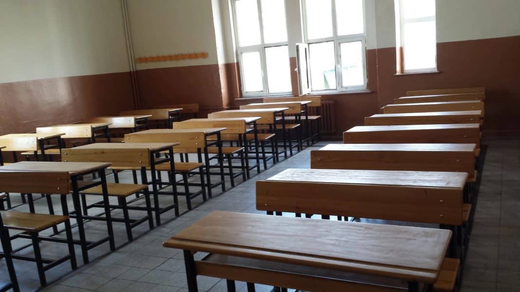 Puste ławki i biurka w szkolnej klasie z otwartymi oknami, brak uczniów.