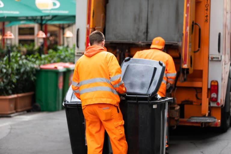 Pracownicy służb komunalnych opróżniają pojemniki na odpady na ulicy w Mrągowie.