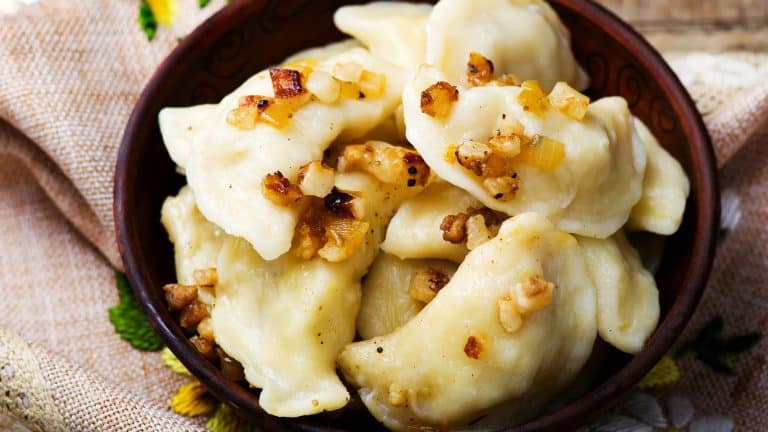 Talerz z pierogami z mięsem i cebulą, podany na drewnianym stole.