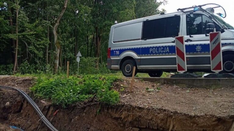 Na zdjęciu teren budowy z policyjnym samochodem na tle drzew, barierkami i wykopem.