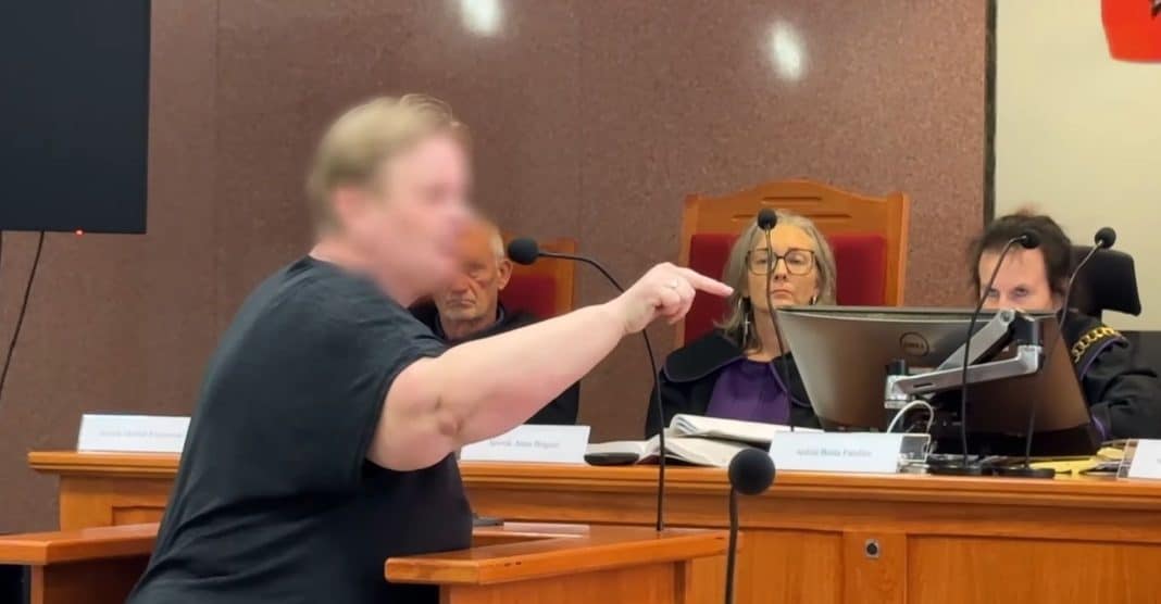 Osoba na sali sądowej przemawia do sędziów, w tle sędzia i inni uczestnicy procesu.