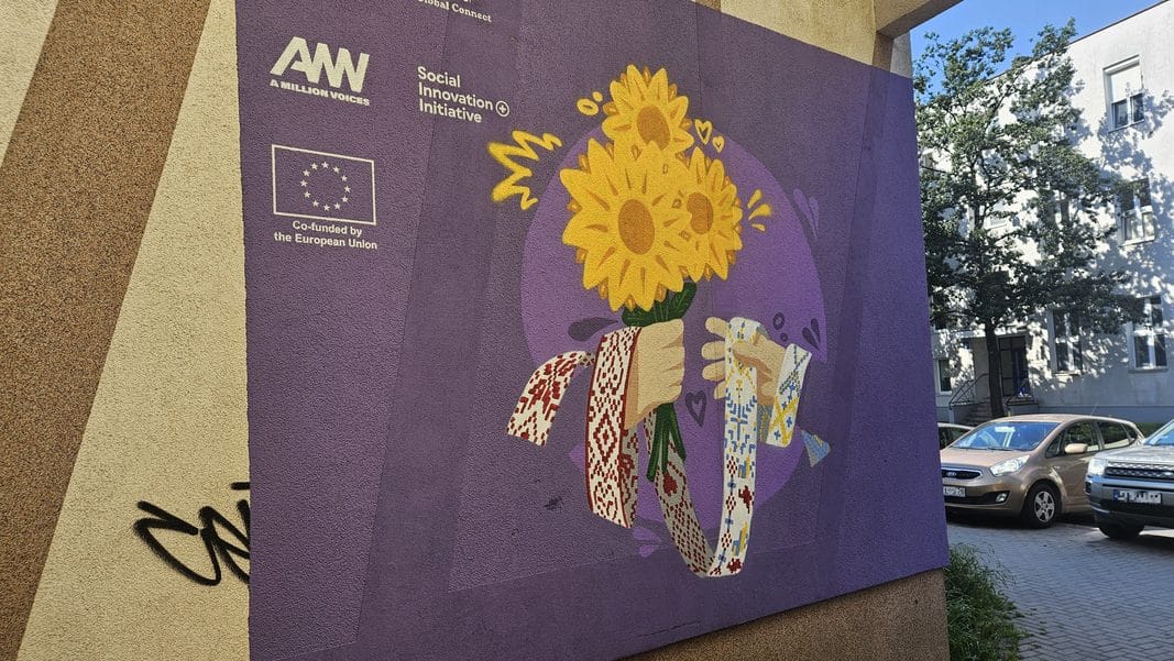 Kolorowy mural na ścianie budynku z kwiatami i rękami, symbolizujący historię uchodźców, przy ul. Jagiellońskiej 18 w Olsztynie.