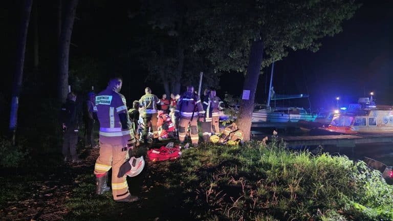 Akcja ratunkowa na Mazurach przy użyciu służb ratowniczych i łodzi, w nocy, wokół drzew i wody.