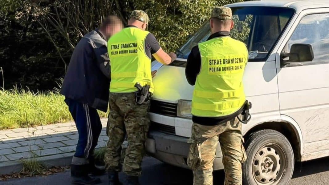 Trzech funkcjonariuszy Straży Granicznej sprawdza dokumenty przy białym busie na drodze.
