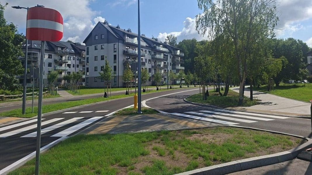 Nowy odcinek drogi w Olsztynie z chodnikami i oznakowaniem, w tle osiedle mieszkaniowe.