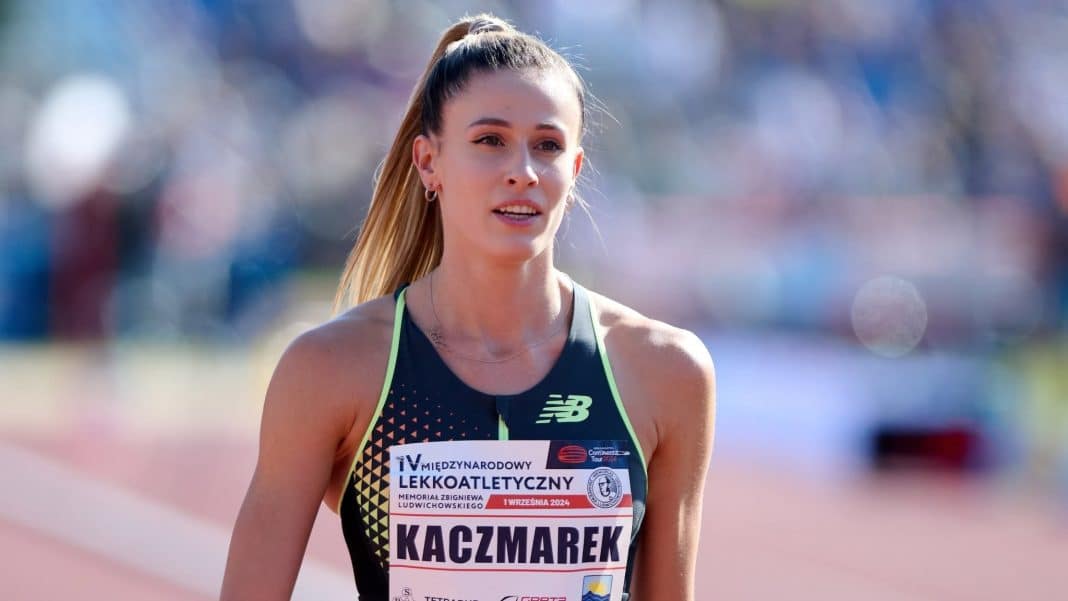 Zdjęcie kobiety w sportowym stroju na bieżni, z długimi blond włosami, w tle rozmyte tłumy.