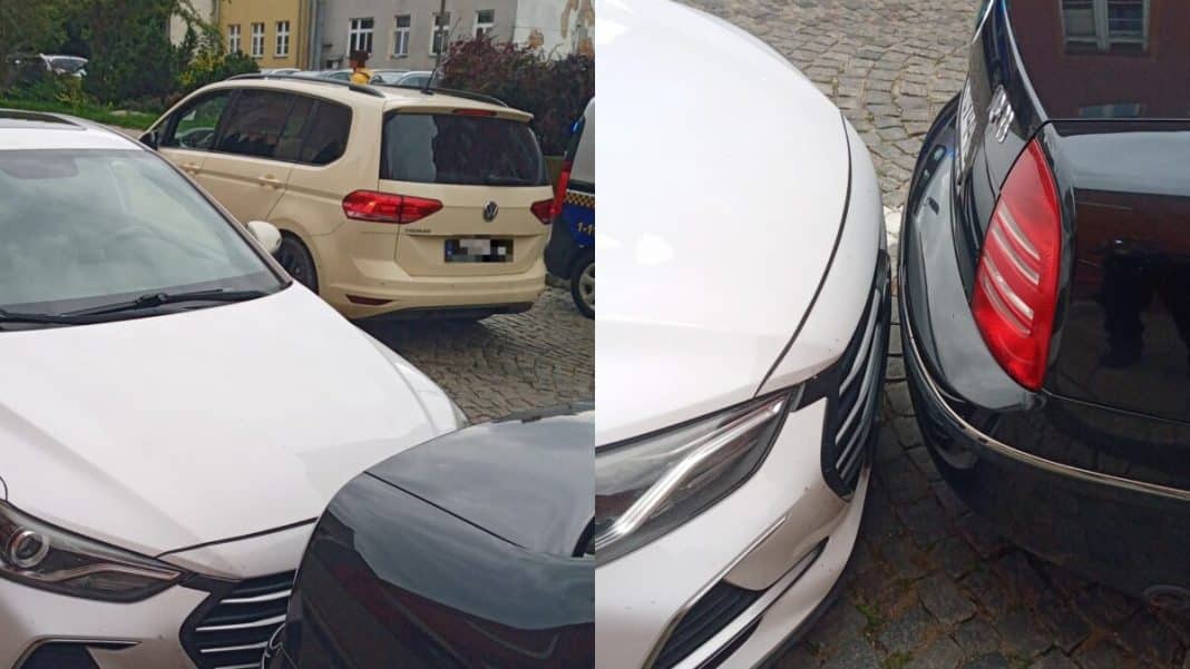 Zdjęcie przedstawia zaparkowane samochody na wąskim parkingu w centrum Olsztyna, z widocznymi przeszkodami w manewrowaniu.