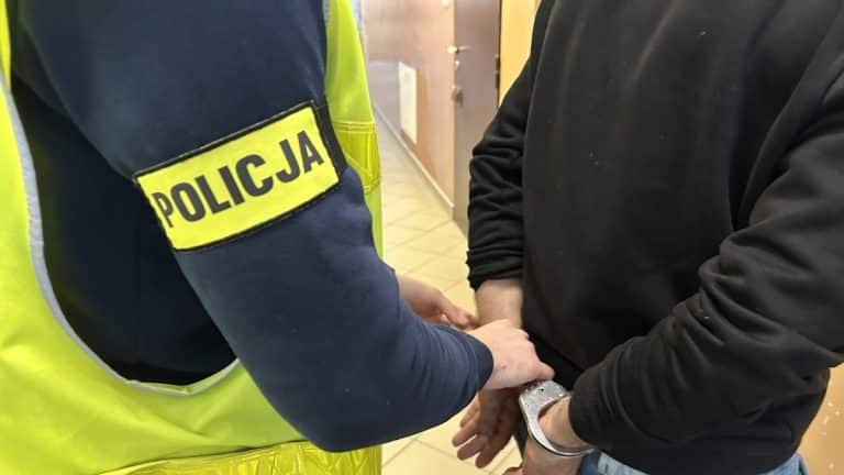 Policjant zatrzymuje mężczyznę z rękami w kajdankach w pomieszczeniu.