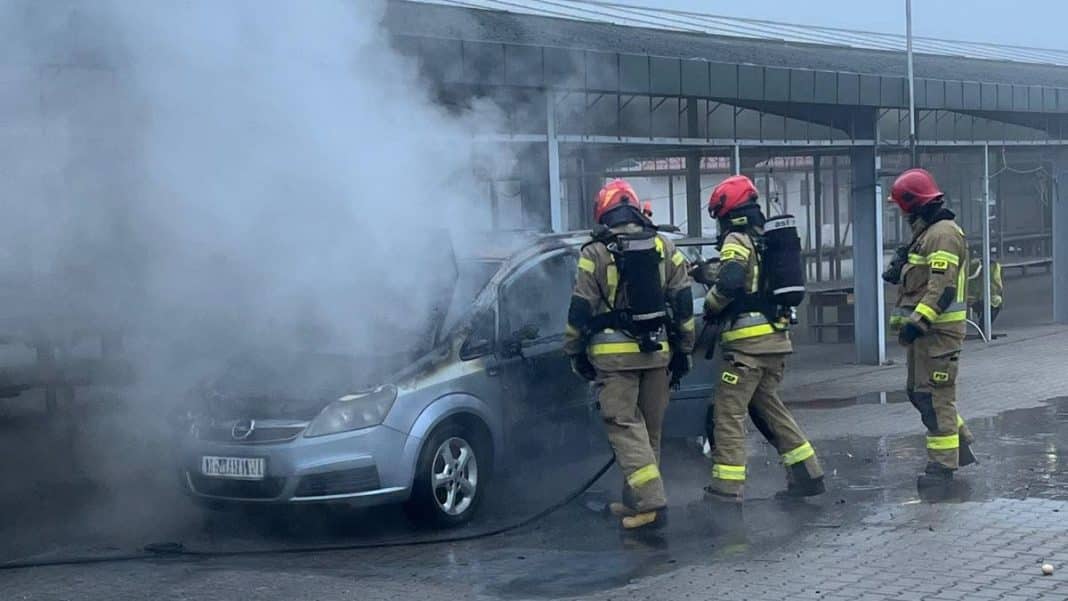 Strażacy gaszą pożar samochodu na targowisku miejskim przy ul. Żeromskiego, w tle hala targowa.