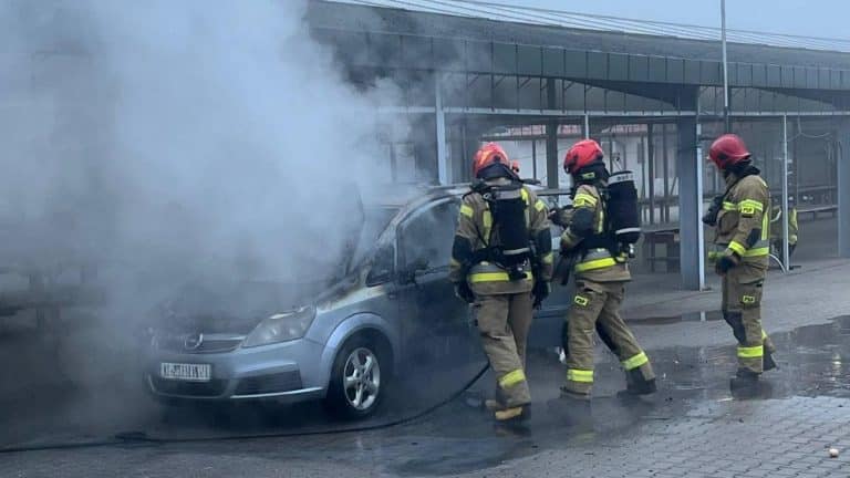 Strażacy gaszą pożar samochodu na targowisku miejskim przy ul. Żeromskiego, w tle hala targowa.
