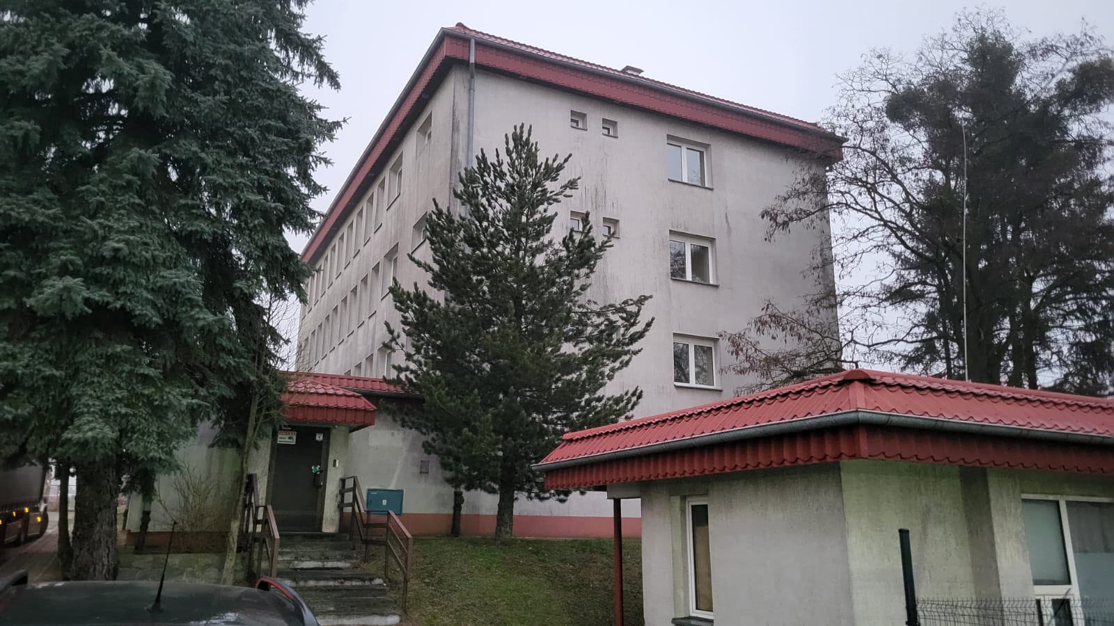 Wielopiętrowy budynek w Olsztynie z otaczającymi drzewami, widoczny od strony ulicy.