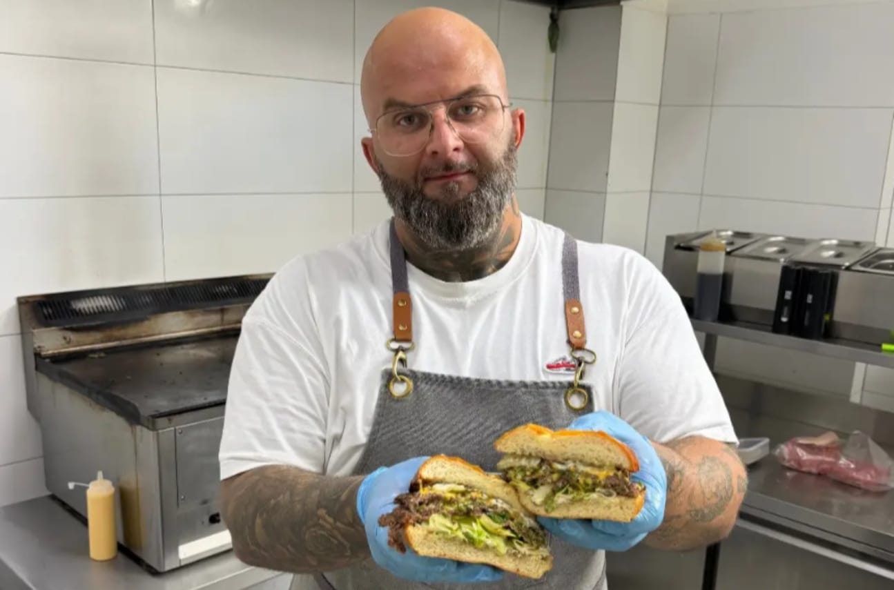 Mężczyzna w kuchni trzymający dwa burgery z podwójną wołowiną i serem cheddar.