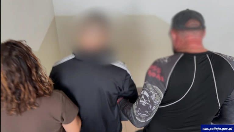 Mężczyzna zatrzymany przez policjantów podczas interwencji na SOR-ze, z widocznym zaczerwienieniem twarzy.