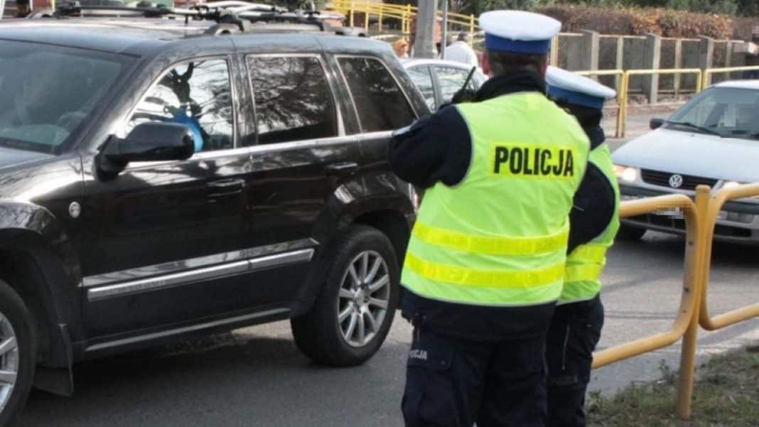 Policjanci na ulicy, w tle samochody i barierki, widać funkcjonariuszy w odblaskowych kamizelkach.