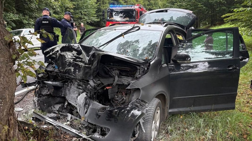 Uszkodzony czarny samochód po wypadku, na miejscu interwencja służb ratunkowych.