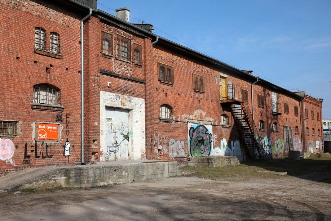 Ceglany budynek z graffiti, z metalową klatką schodową na zewnątrz, na tle nieba.