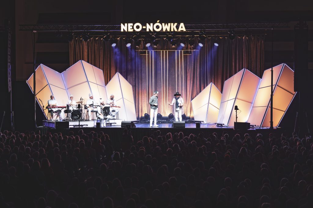 Widownia ogląda występ kabaretu Neo-Nówka na scenie z dużymi, geometrycznymi dekoracjami i oświetleniem.
