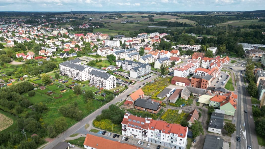 Widok na osiedle mieszkaniowe z wielopiętrowymi budynkami i domami jednorodzinnymi, otoczone zielenią.