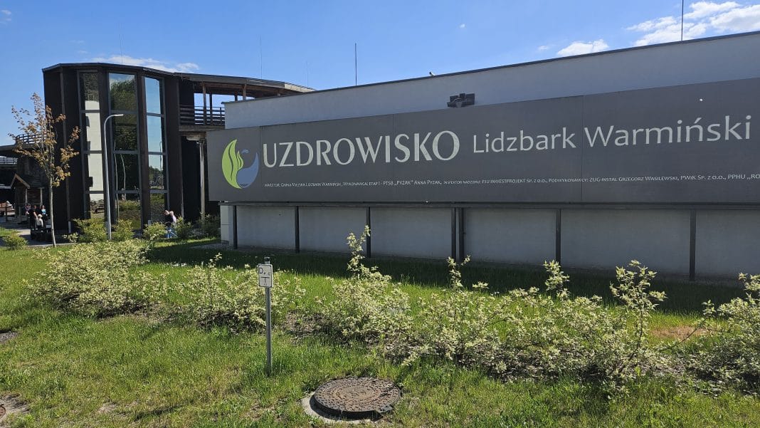 Widok na odnowione uzdrowisko w Lidzbarku Warmińskim z dużym napisem na ścianie.