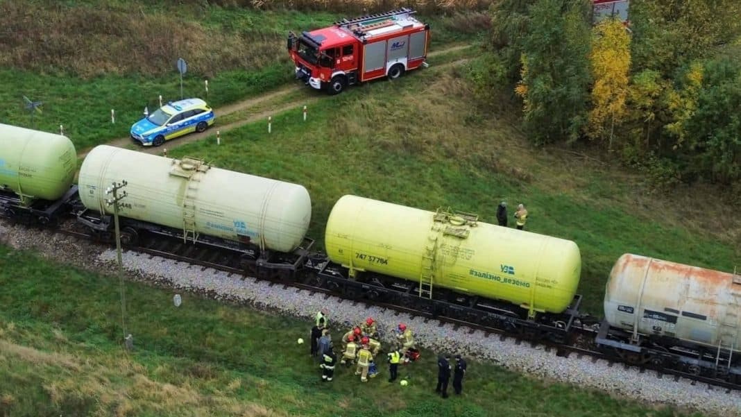 Straż pożarna i policja na miejscu zdarzenia przy torach kolejowych, wokół wagony cystern, w pobliżu lasu.