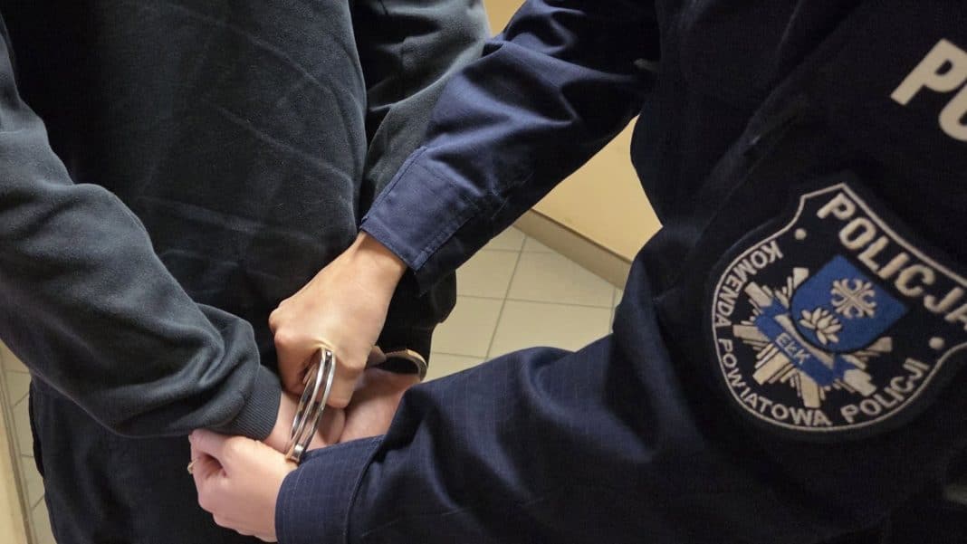 Policjant trzyma ręce ucznia w kajdankach podczas zatrzymania.