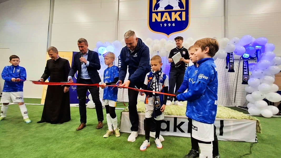 Dzieci i dorośli podczas oficjalnego otwarcia nowej hali piłkarskiej w Olsztynie, z logo Naki Football Park w tle.