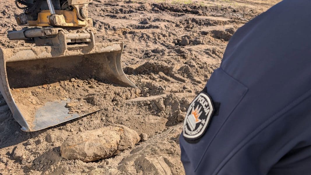Pracownik policji stoi obok wykopanej bomby lotniczej w ziemi podczas akcji w Gołdapi.