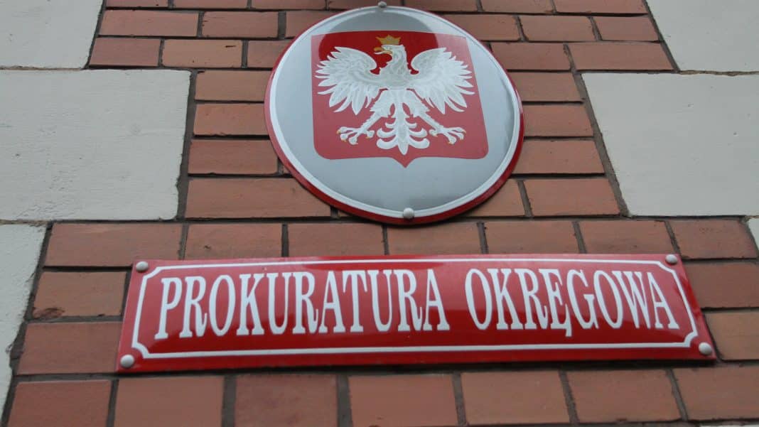Zdjęcie tablicy z herbem Polski i napisem 'Prokuratura Okręgowa' na ceglanej ścianie.
