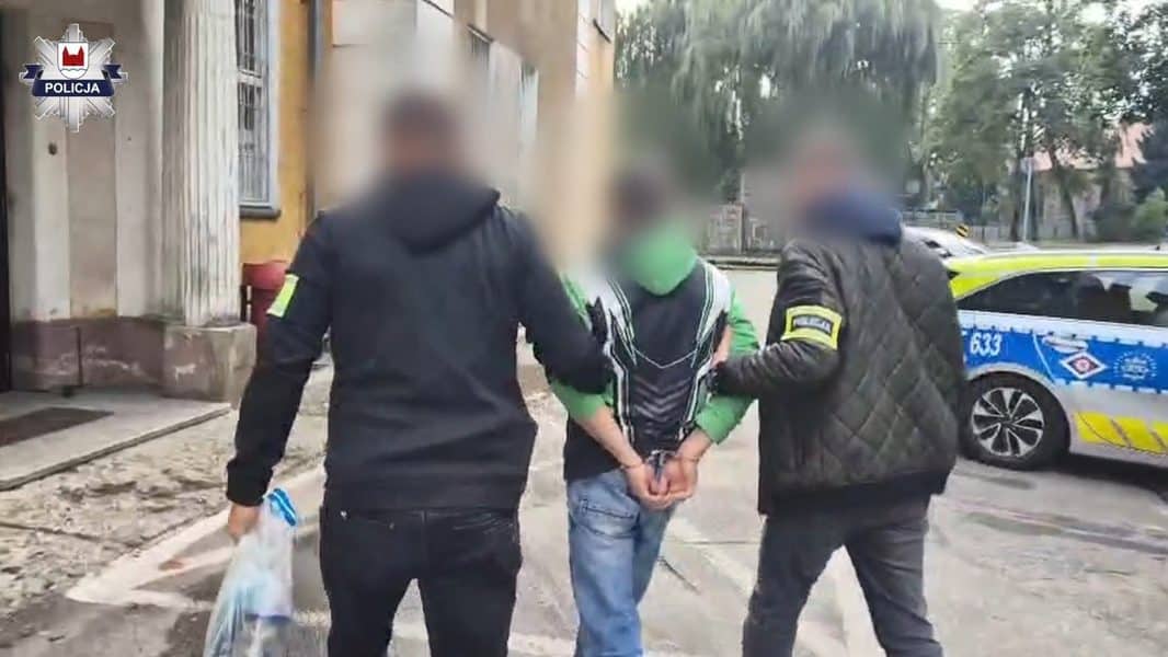 Trzech mężczyzn zatrzymanych przez policję, jeden z nich w rękach funkcjonariuszy, w tle radiowóz policyjny.