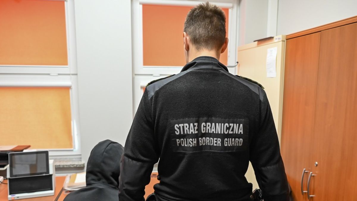 Funkcjonariusz Straży Granicznej rozmawia z kierowcą w pomieszczeniu służbowym.