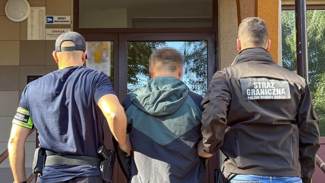 Mężczyzna zatrzymany przez straż graniczną przed wejściem do budynku, z tyłu widoczne drzwi i okno.