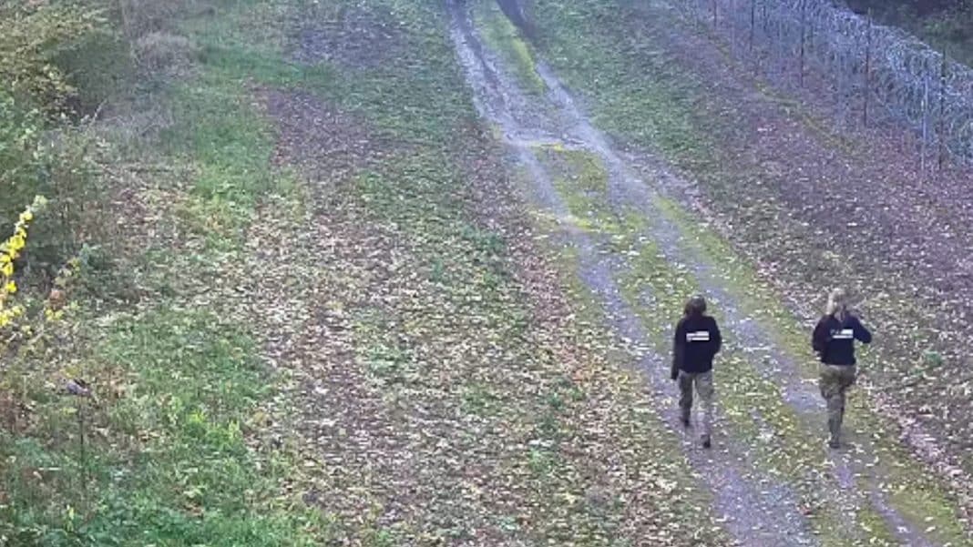 Dwoje turystów z Belgii na drodze granicznej przy granicy z Rosją, w tle zalesiony teren.