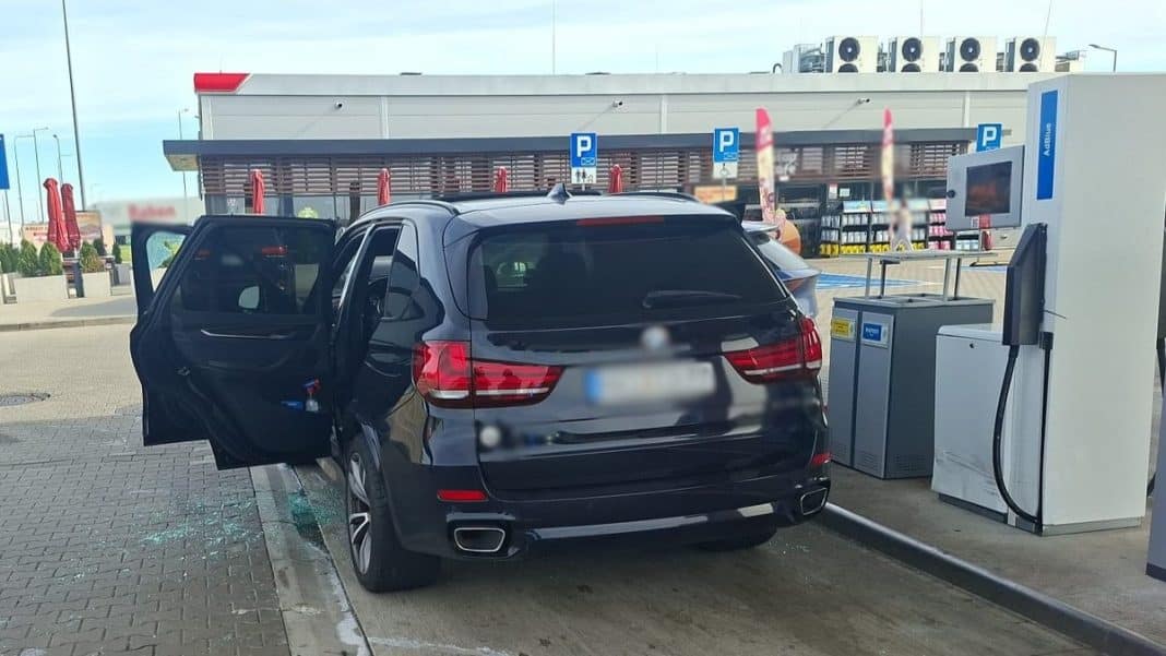 Czarny SUV na stacji benzynowej z otwartymi drzwiami, w tle parking i budynek.