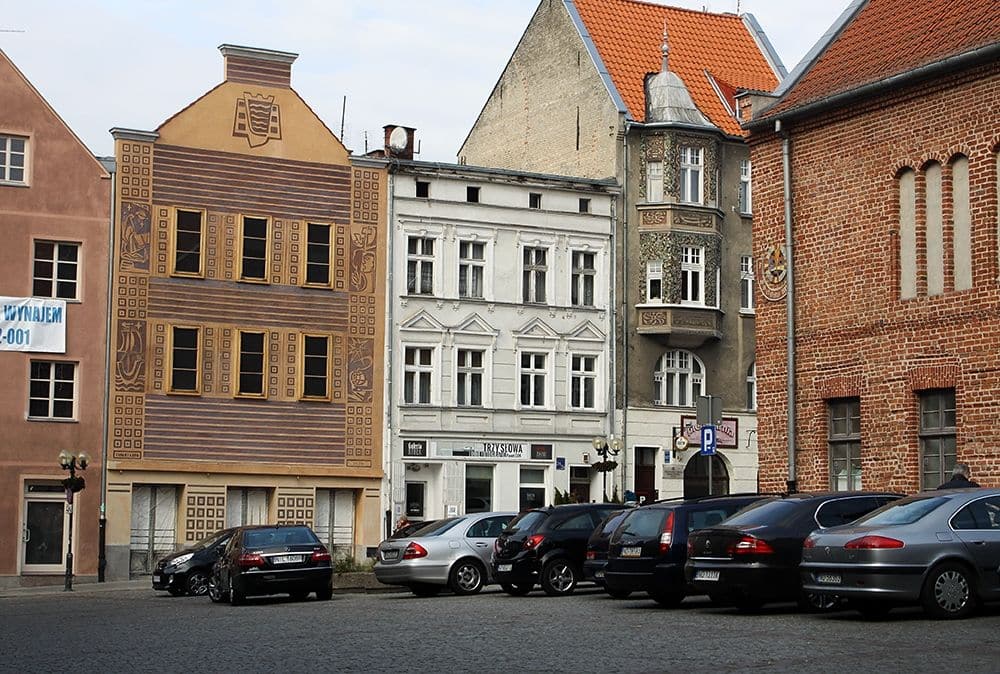 Widok na zabytkowe budynki na Starym Mieście w Olsztynie, w tym jeden z ozdobnym malowaniem na fasadzie.