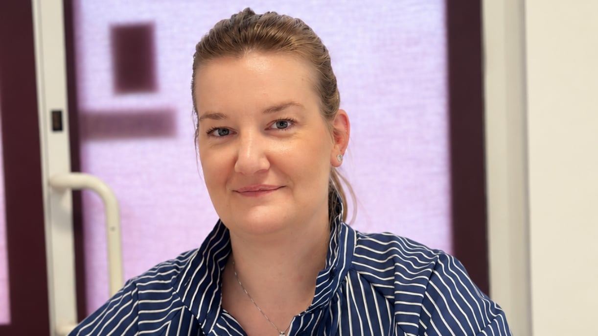 Uśmiechnięta kobieta w biurze poradni psychologiczno-pedagogicznej, za nią drzwi wejściowe.