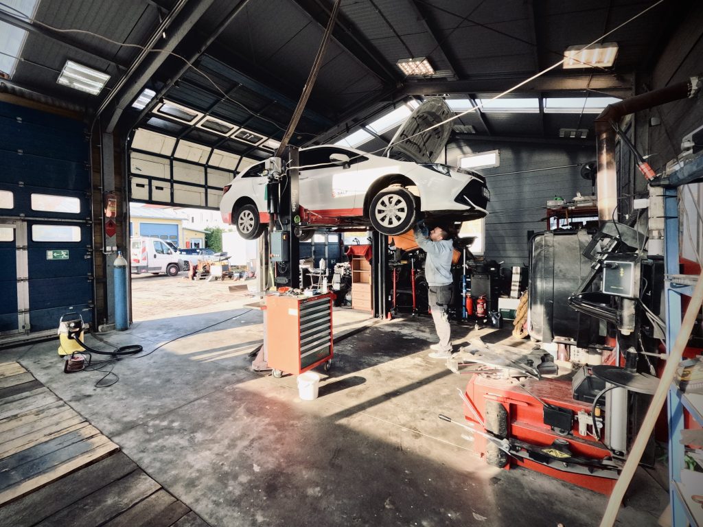Wewnątrz nowego warsztatu samochodowego z podniesionym samochodem i pracującym mechanikiem.