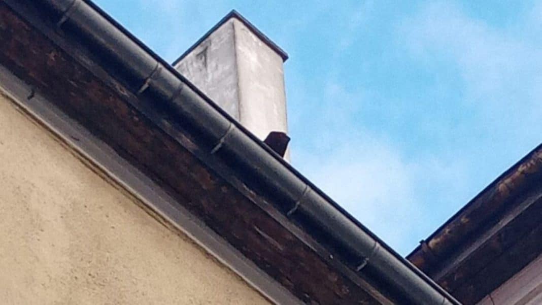 Zdjęcie dachu budynku z widocznymi spadającymi dachówkami i niebieskim niebem w tle.