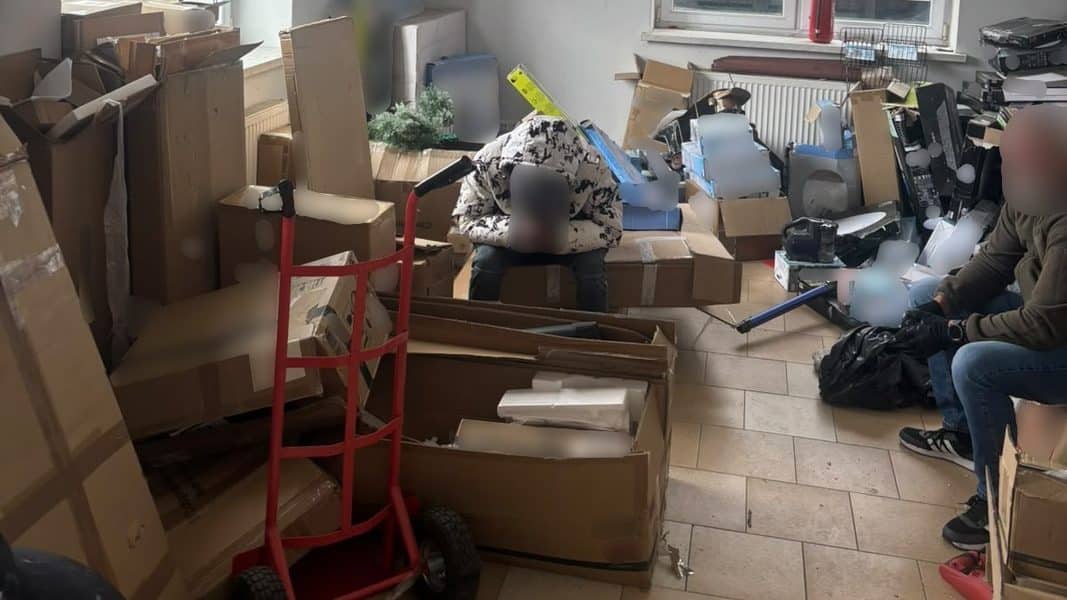 Pomieszczenie pełne kartonów, sprzętu i osób podczas akcji służb na Warmii i Mazurach.