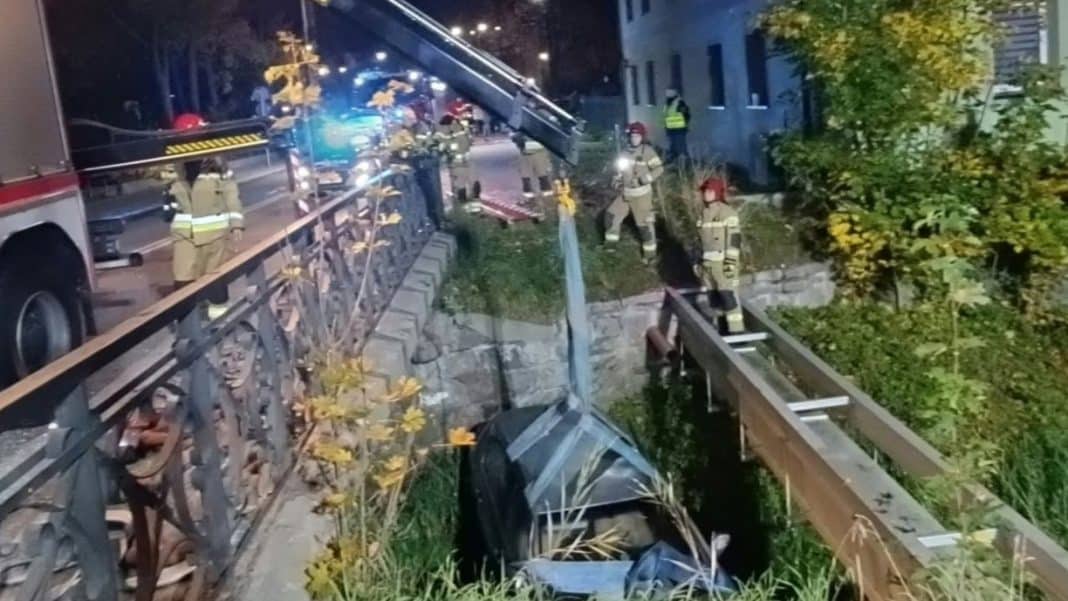 Samochód wpadł do rzeki po spadnięciu z mostu, na miejscu strażacy przygotowują się do wyciągnięcia auta.