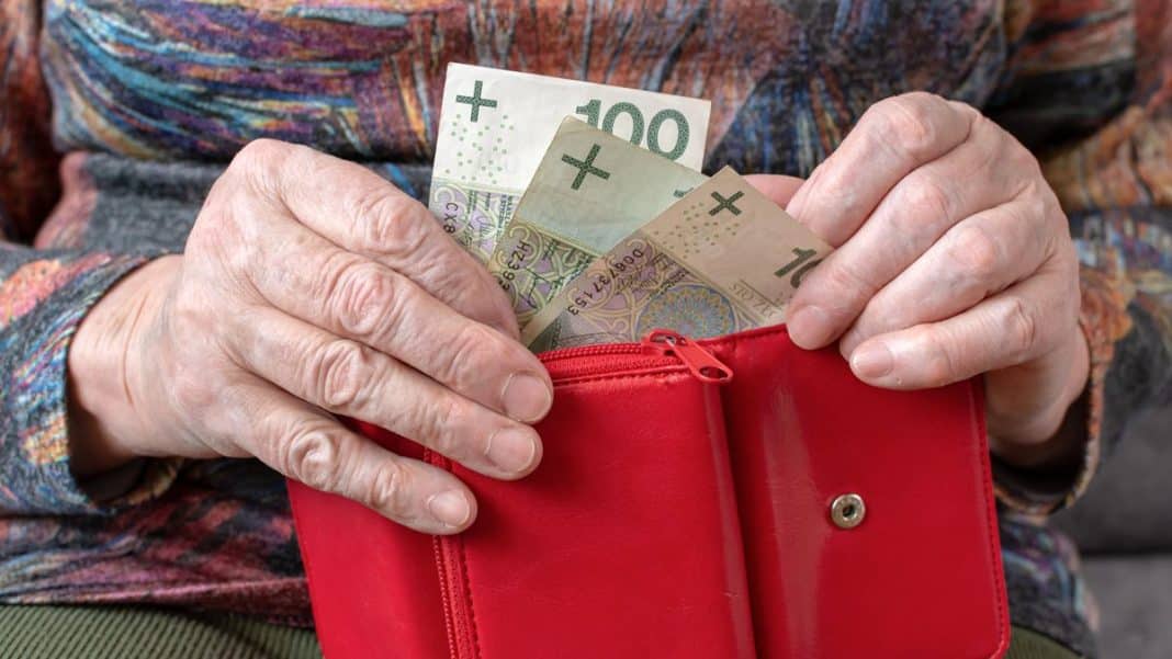 Dłoń osoby wkładającej banknoty do czerwonego portfela, na tle odzieży w kolorowe wzory.