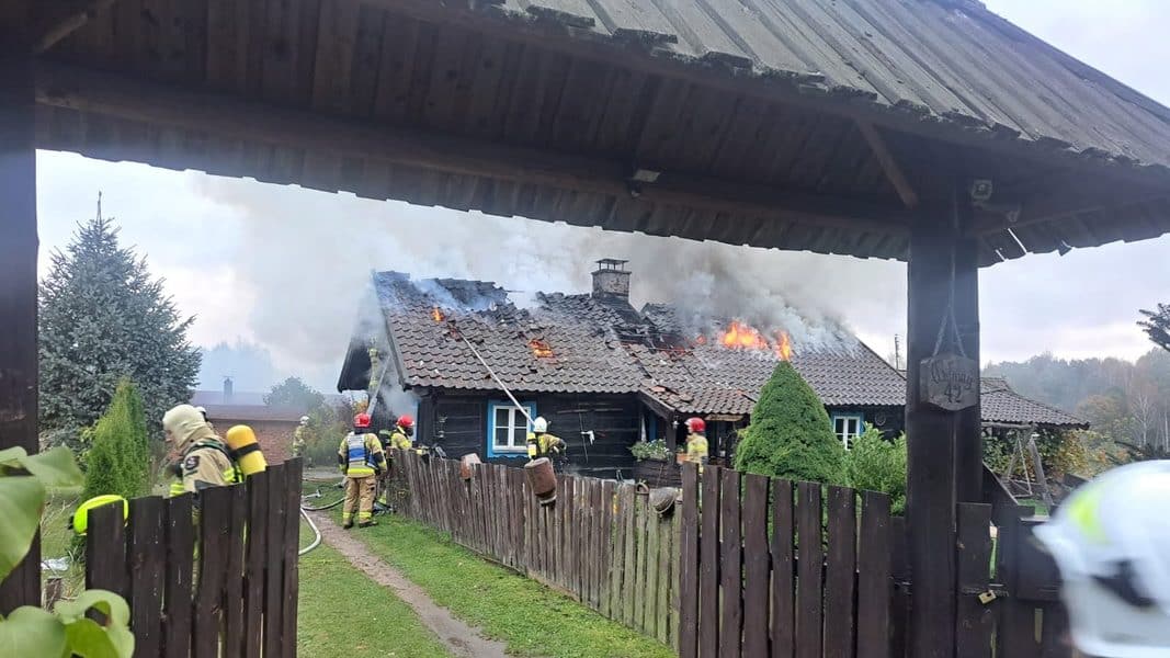 Pożar domu pod Olsztynem, ogień obejmuje cały dach, na miejscu straż pożarna z wieloma zastępami.