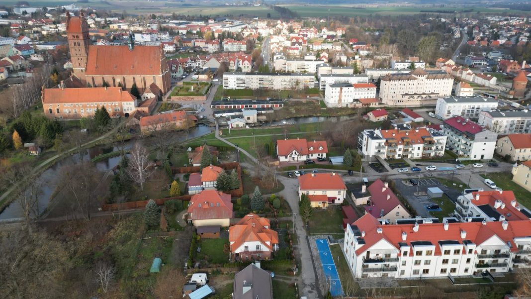 Widok na centrum miasta z drona, z widocznymi budynkami, kościołem i zielonymi terenami nad rzeką.