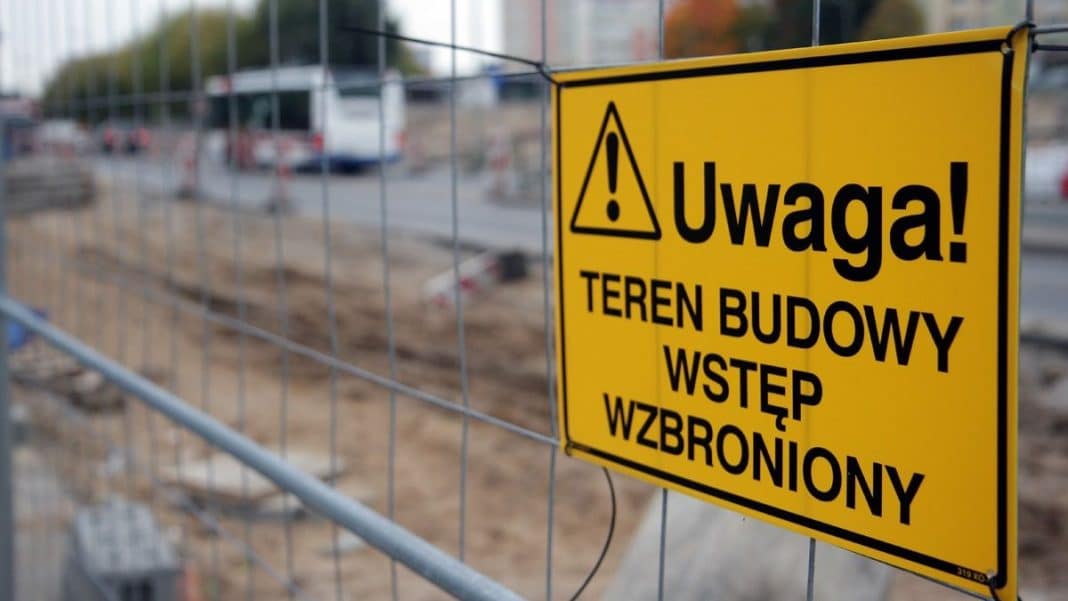 Żółta tablica ostrzegawcza na placu budowy z napisem 'Uwaga! Teren budowy wstęp wzbroniony'.