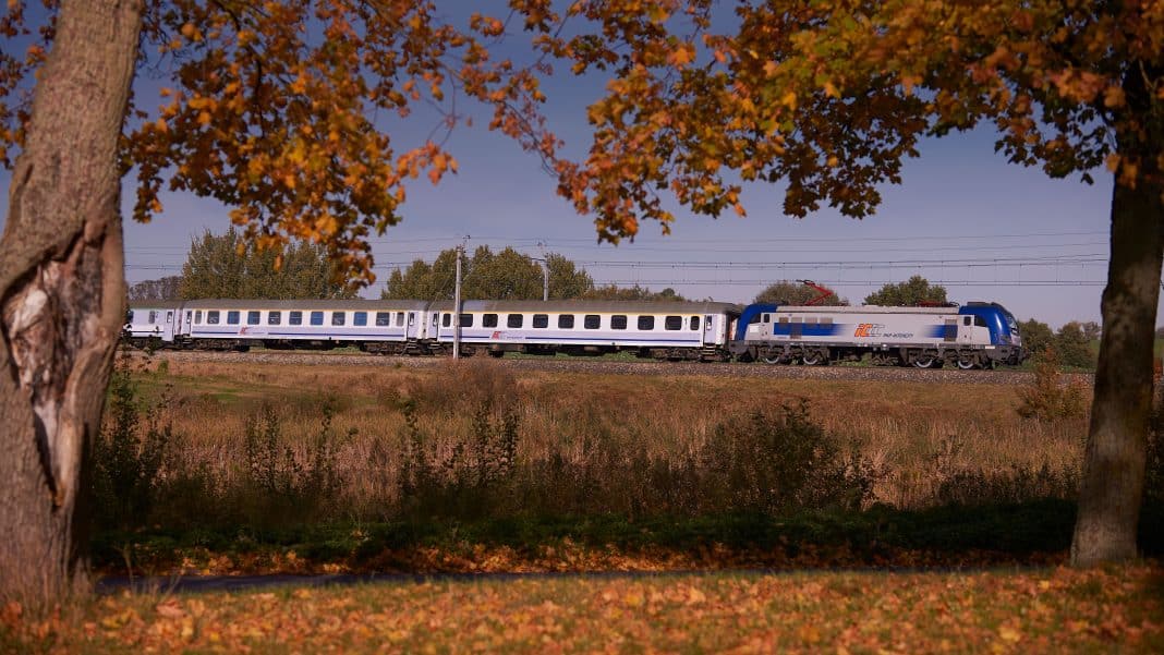 Pociąg PKP Intercity na tle jesiennego krajobrazu z drzewami o kolorowych liściach.