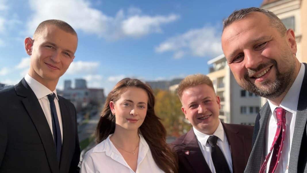 Grupa studentów i przedstawiciel władz Olsztyna podczas spotkania na zewnątrz budynku, uśmiechnięci i w formalnych ubraniach.